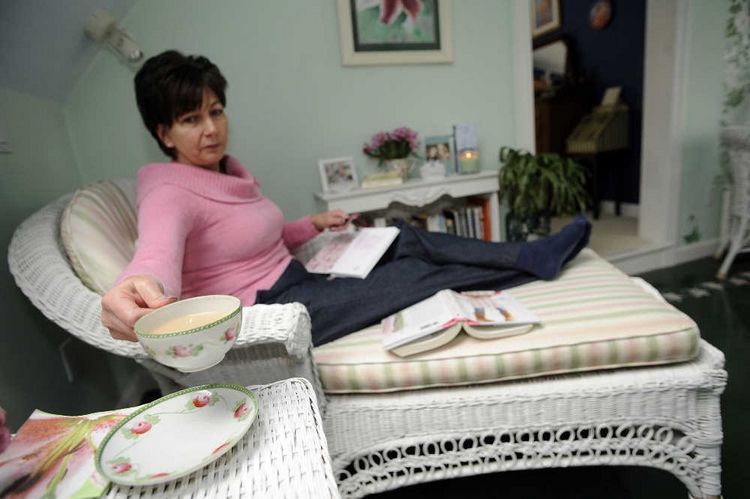 Marie in her Nurturing Space as seen in the Worcester T & G Sunday paper featuring an interior designer mom cave. White wicker chaise lounge, pink and green stripe cushions, pink and green floral china teacup.