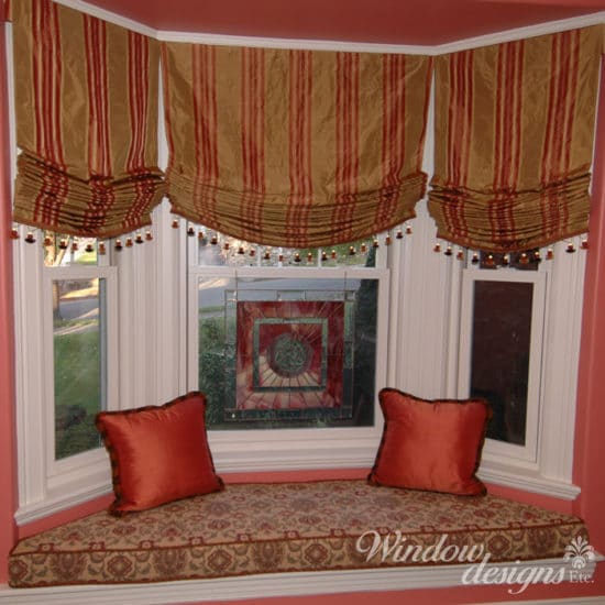 Window seat area in Worcester Craftsman home. Featuring relaxed Roman shades with bead trim. A tapestry window seat cushion, pillows and craftsman stained glass.